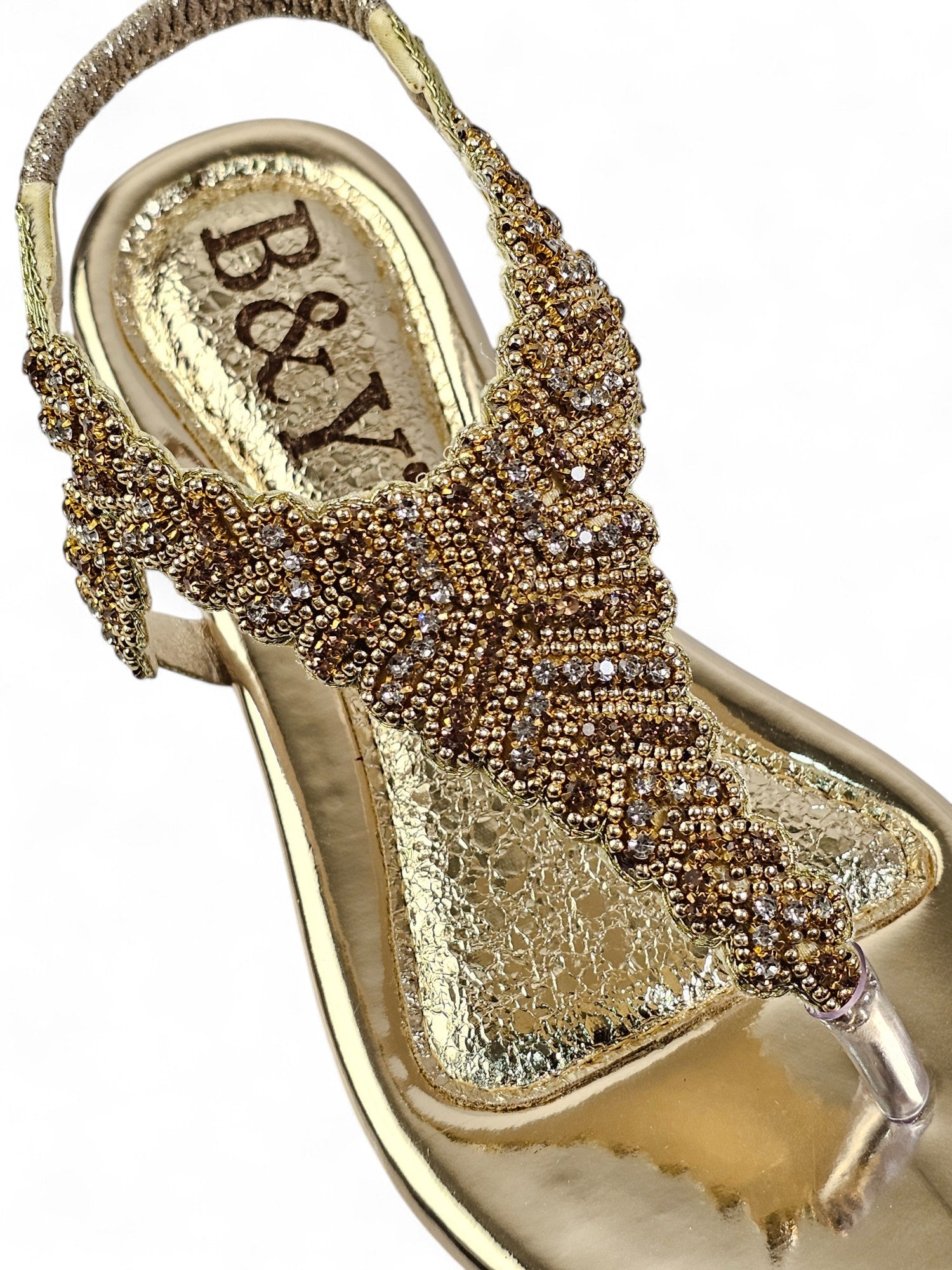A close-up of a gold-colored sandal with a beaded and embellished design.