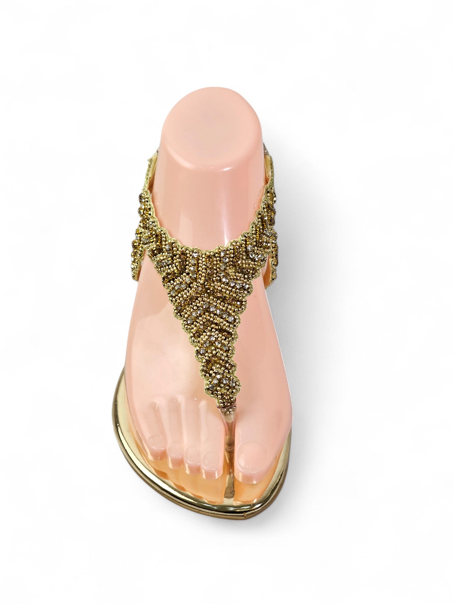 A pink foot model wearing a gold and beaded sandal.
