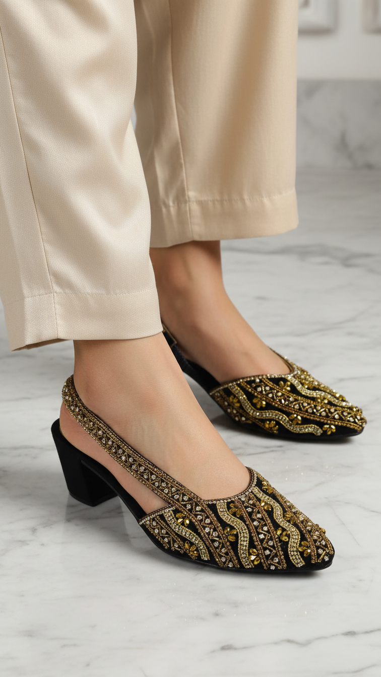 A close-up of a person's feet wearing black and gold embellished shoes on a marble floor.