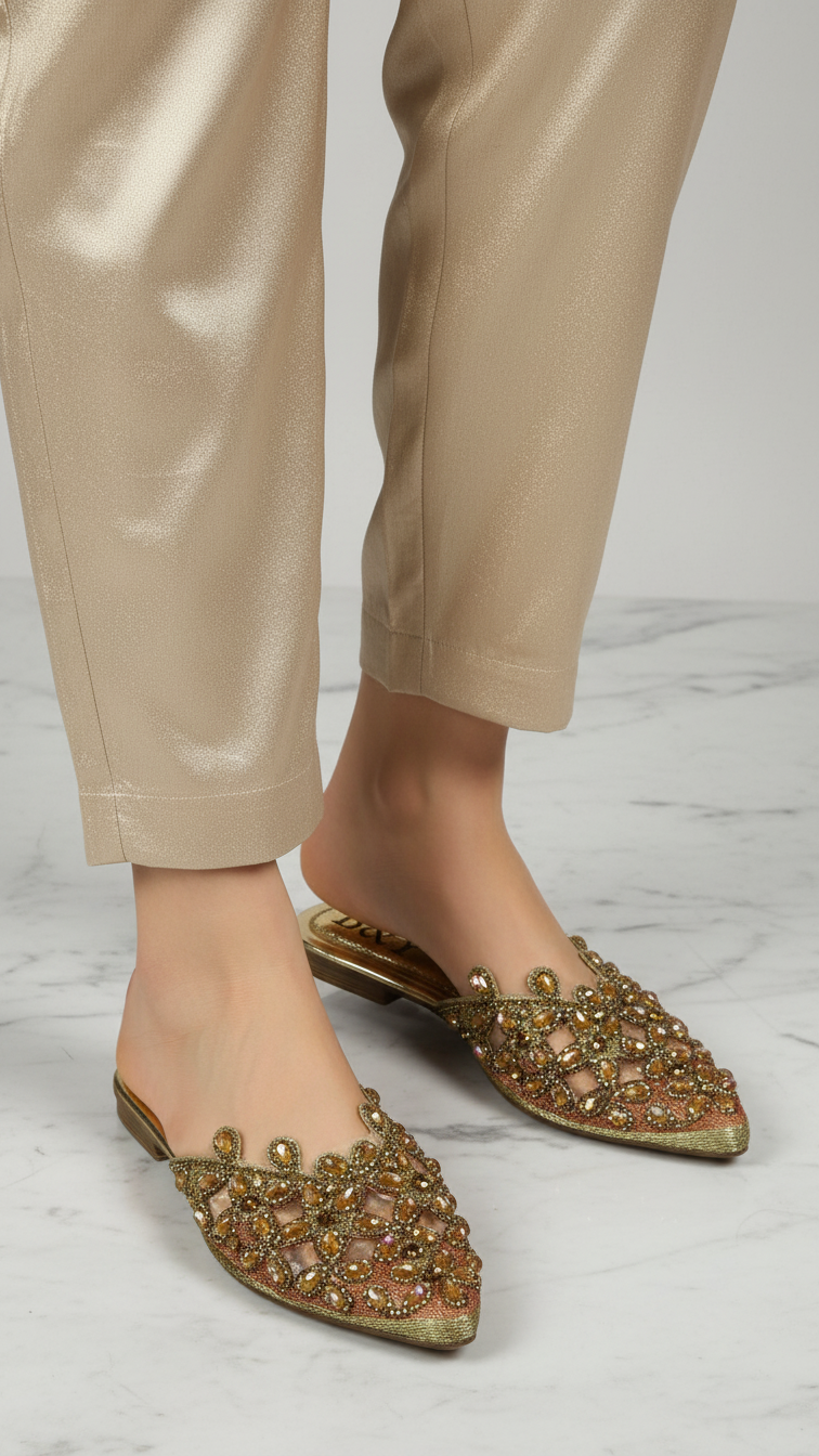 A pair of gold, beige, and gold embellished mules or slippers with intricate designs.