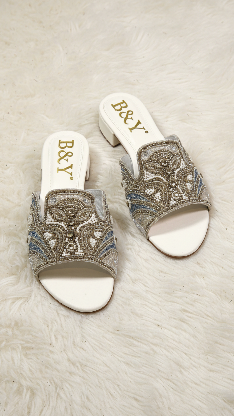 Sandália artesanal B&Y em tom creme com bordado manual em pedrarias douradas, cristais delicados e design floral orgânico, salto baixo e acabamento sofisticado.