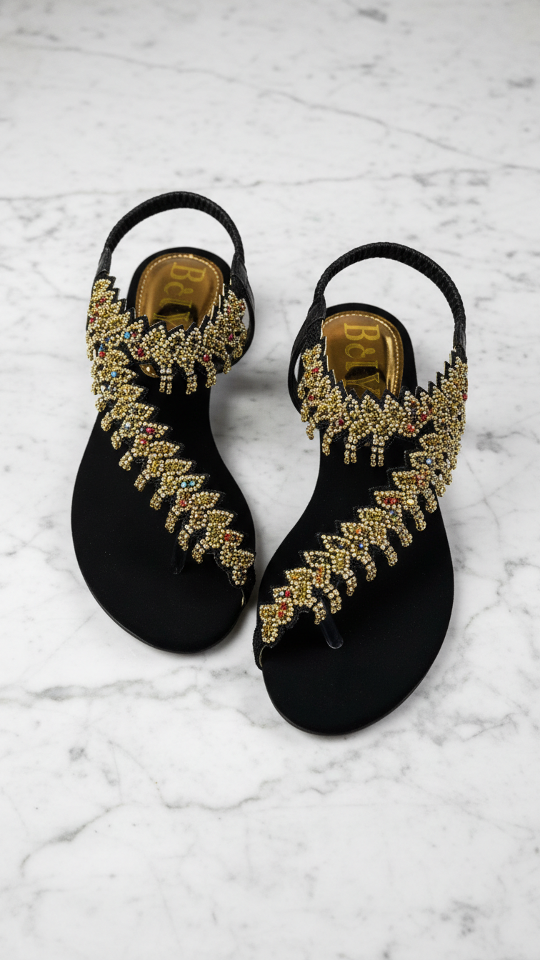 Sandália artesanal B&Y preta com bordado manual em pedrarias douradas e detalhes coloridos, design central sofisticado e salto baixo.