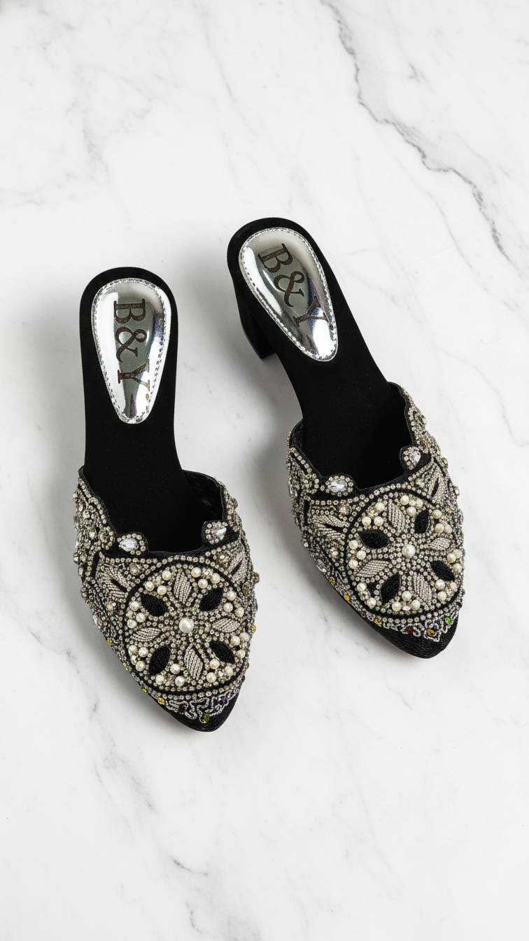 Mule artesanal B&Y preto com bordados manuais em pérolas, pedrarias e fios metálicos prateados e dourados, design geométrico floral e salto médio.