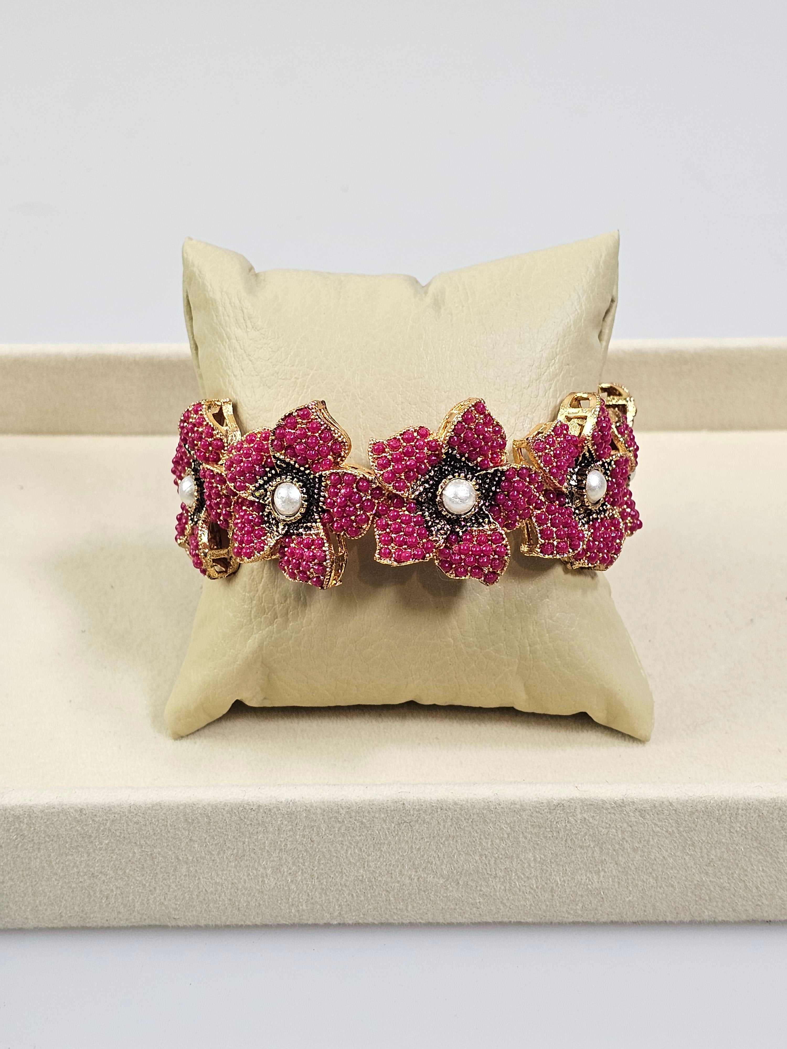 Bracelete floral artesanal B&Y com flores rosa-rubi, detalhes dourados e pérolas centrais.