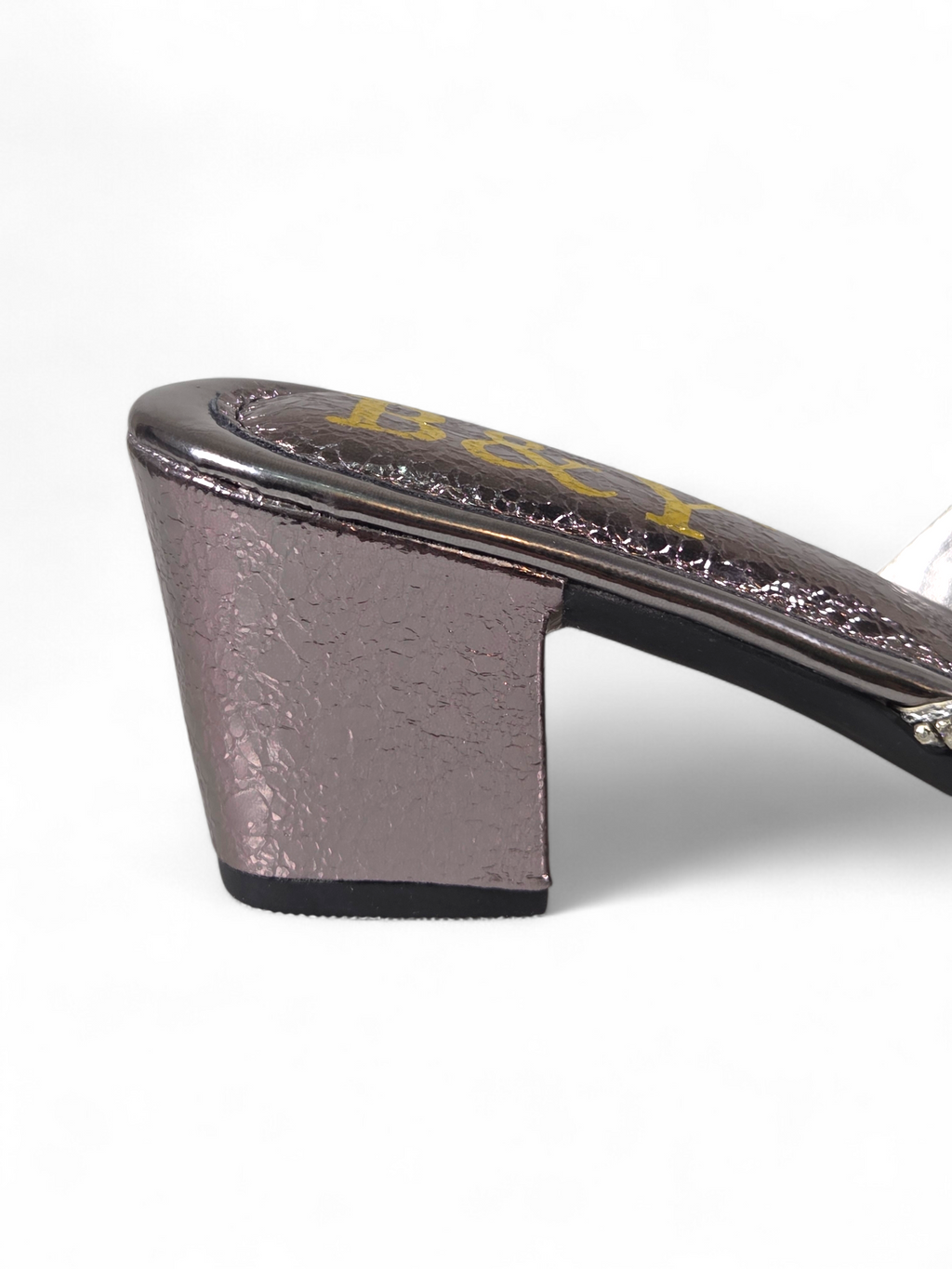 A close-up view of a shiny, metallic heel on a shoe, with a textured surface and a gold-colored design.