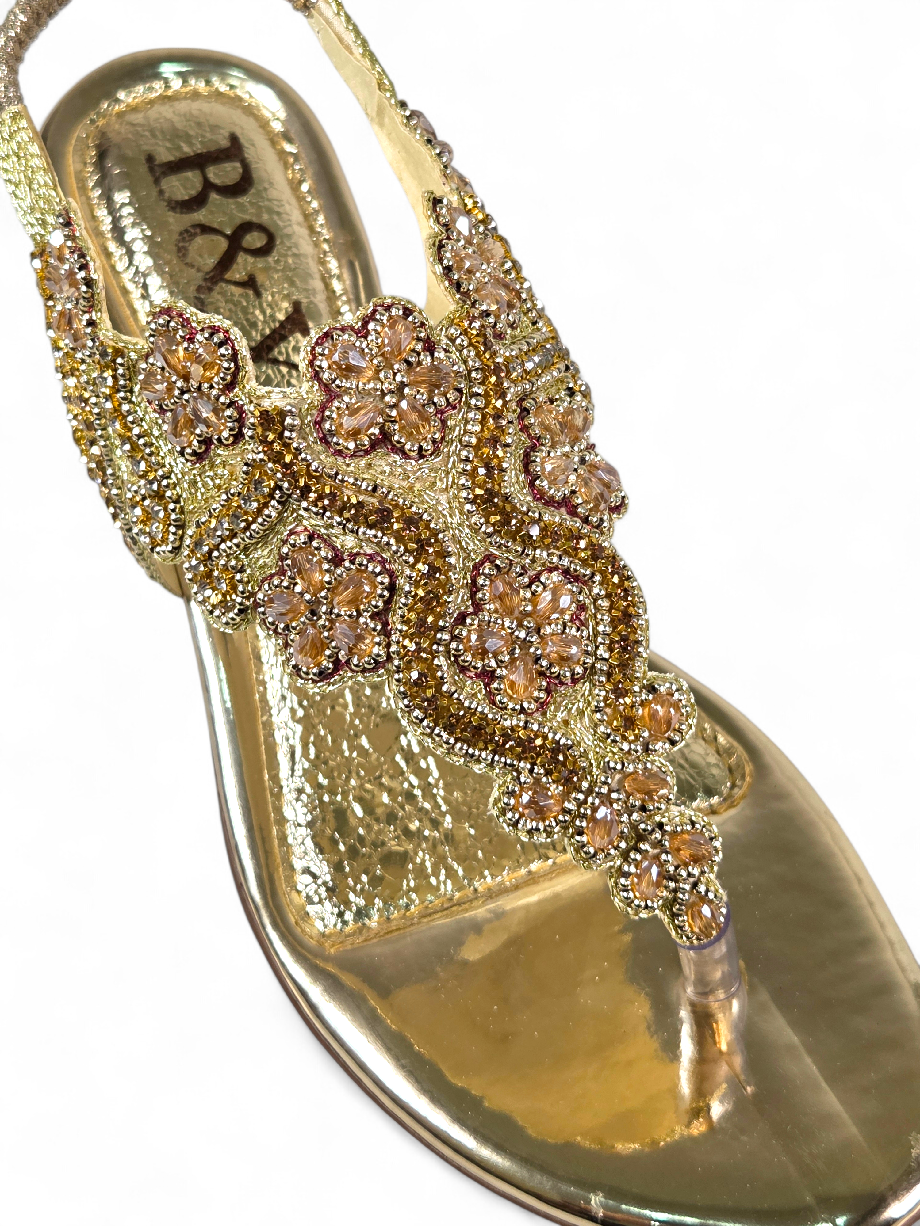 Sandália artesanal B&Y dourada com bordados florais, aplicação de cristais, fechamento no calcanhar e salto baixo, em fundo branco.