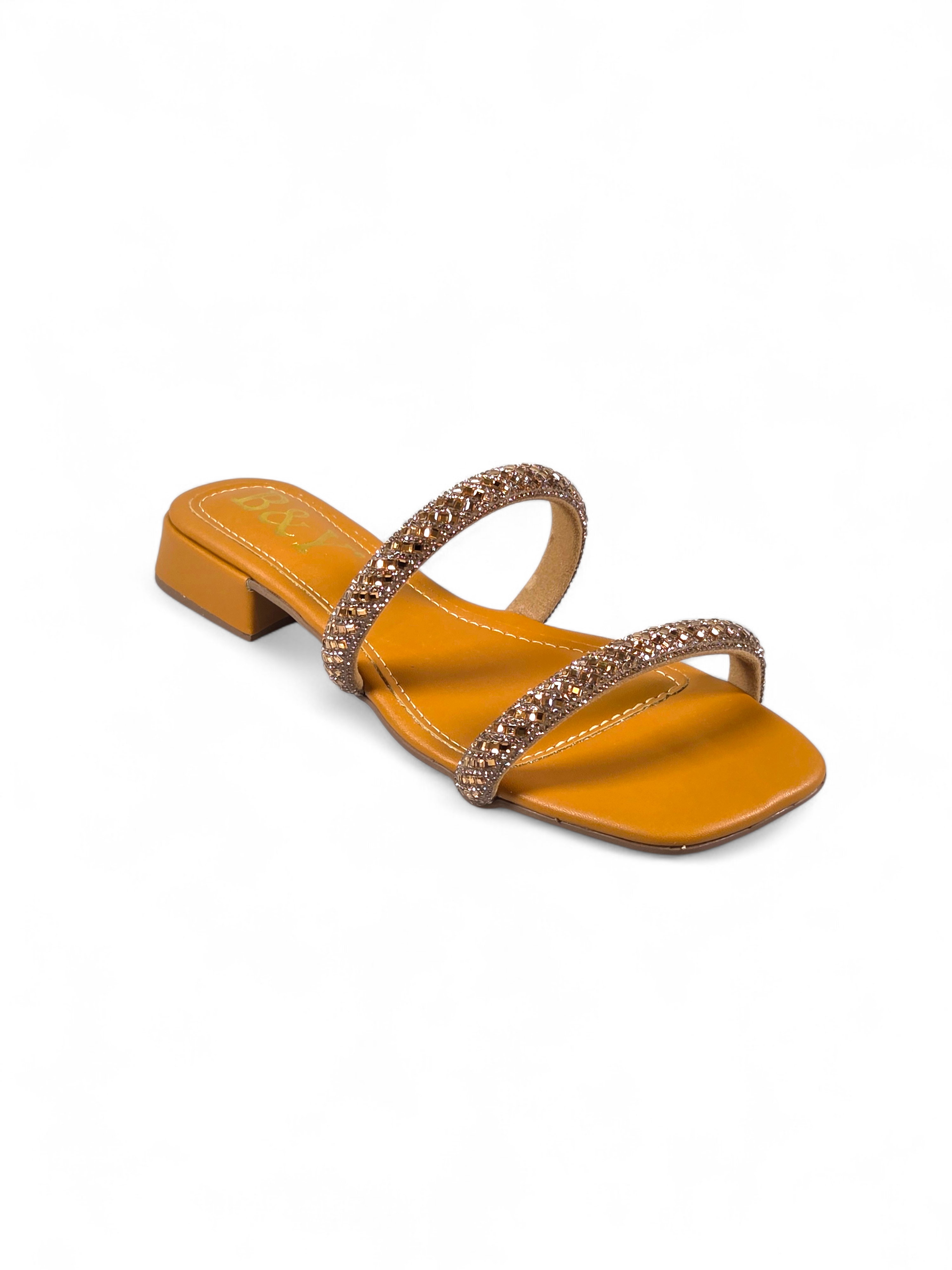 Sandália artesanal B&Y em tom quente com duas tiras cravejadas de cristais, salto baixo e acabamento sofisticado, em fundo branco.