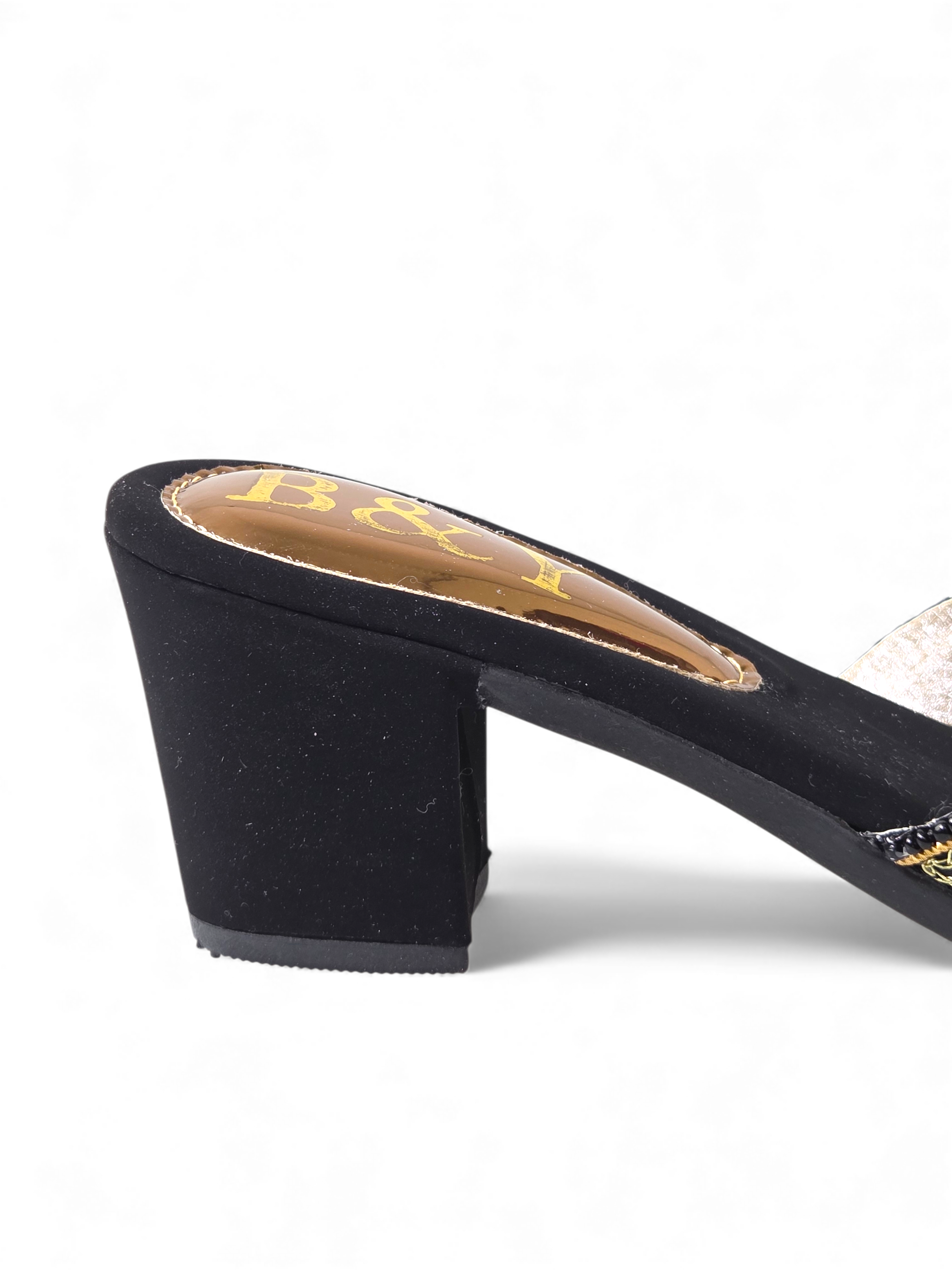 A close-up view of a black high-heeled shoe with a gold heel and the word "B" printed on the heel.