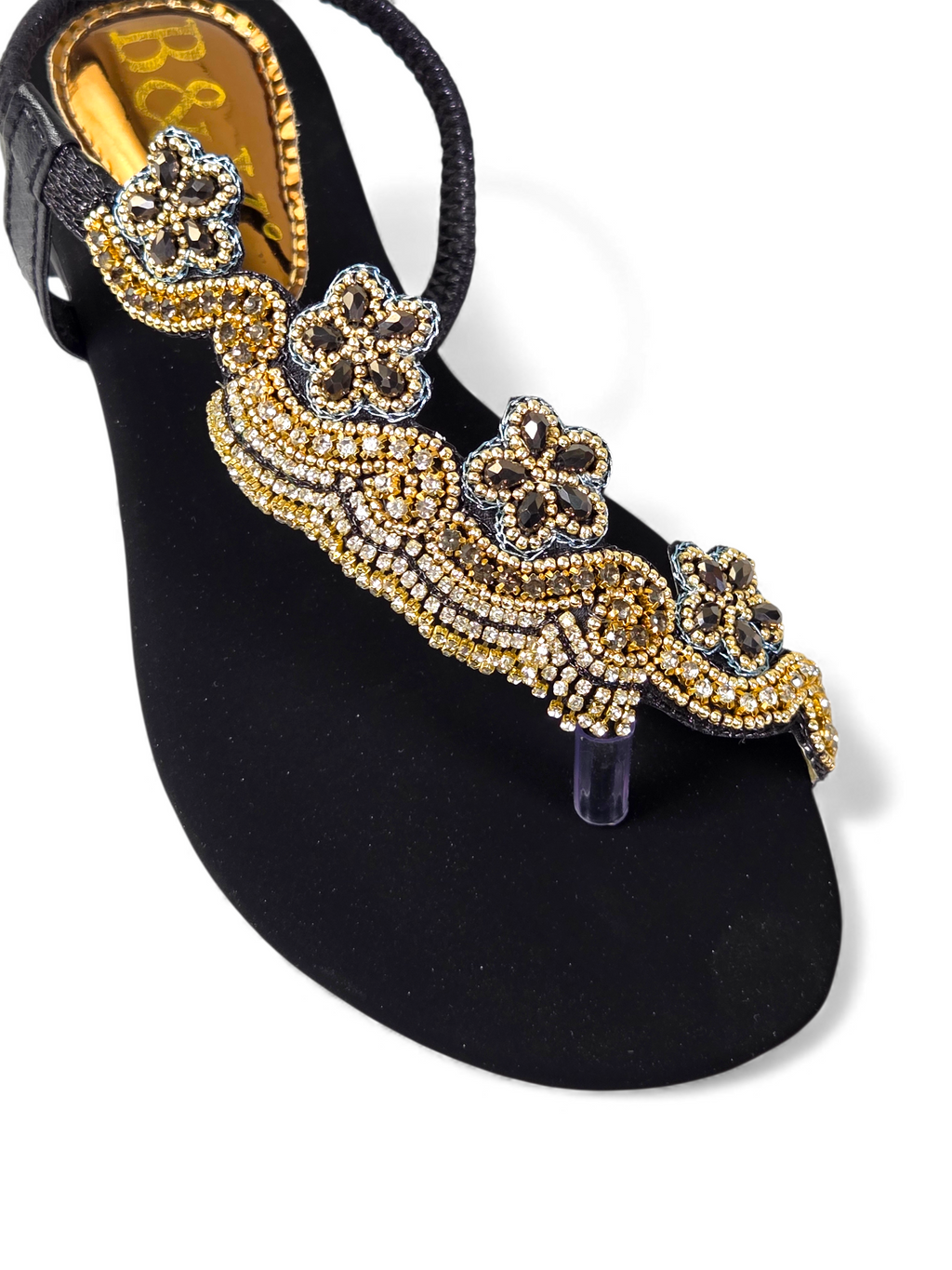 A close-up view of a black, embellished sandal with gold and silver rhinestones or crystals.