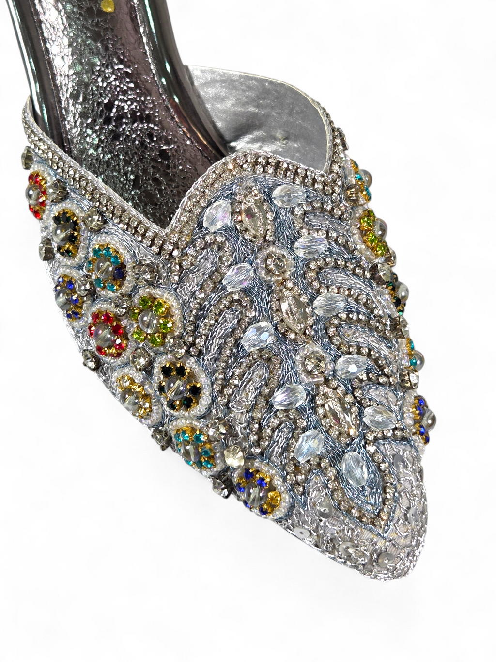 A close-up view of a silver, embellished shoe with a variety of colorful gemstones and intricate designs.