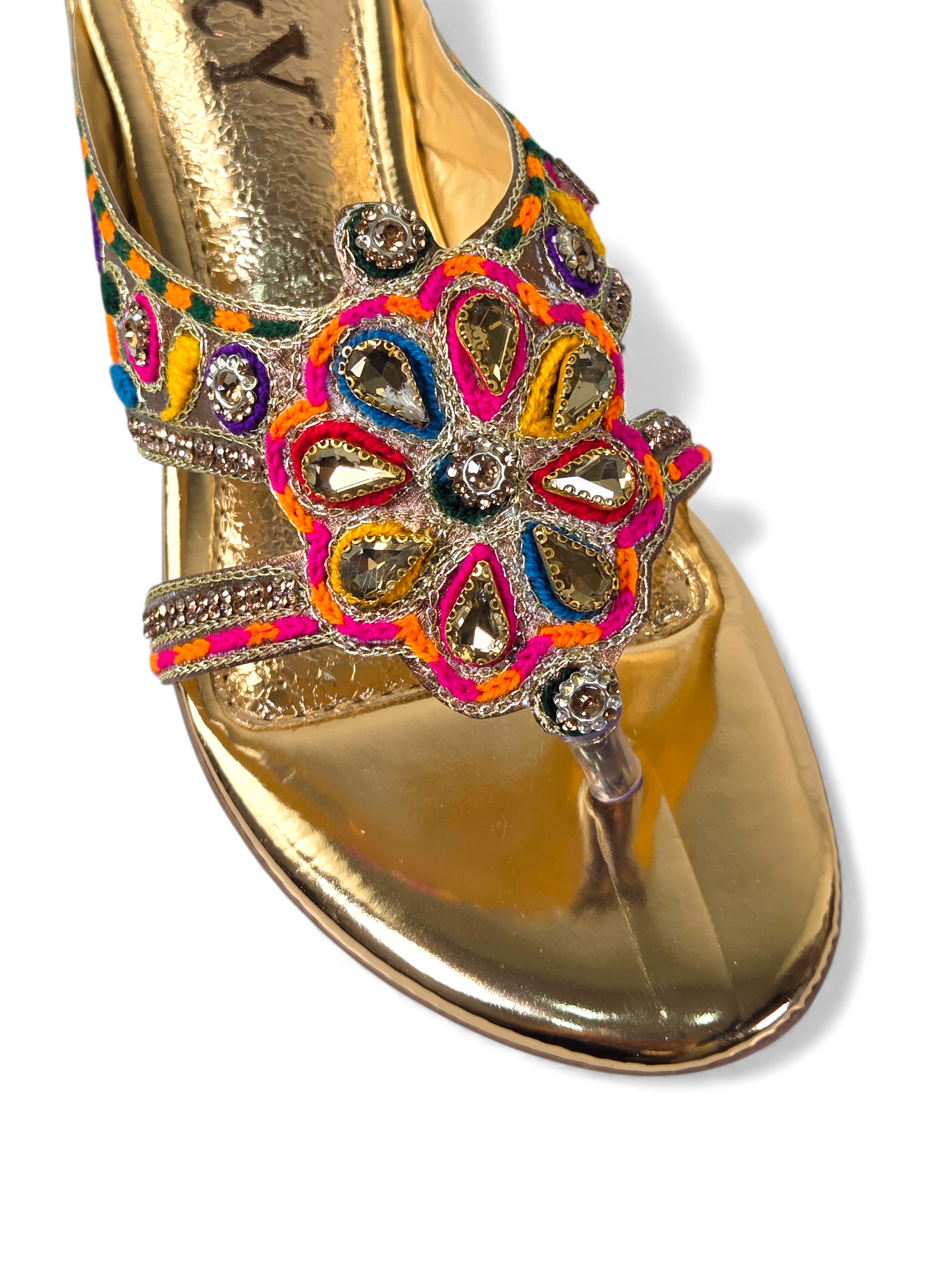 A close-up view of a gold-colored sandal with a decorative floral embellishment on the toe area.