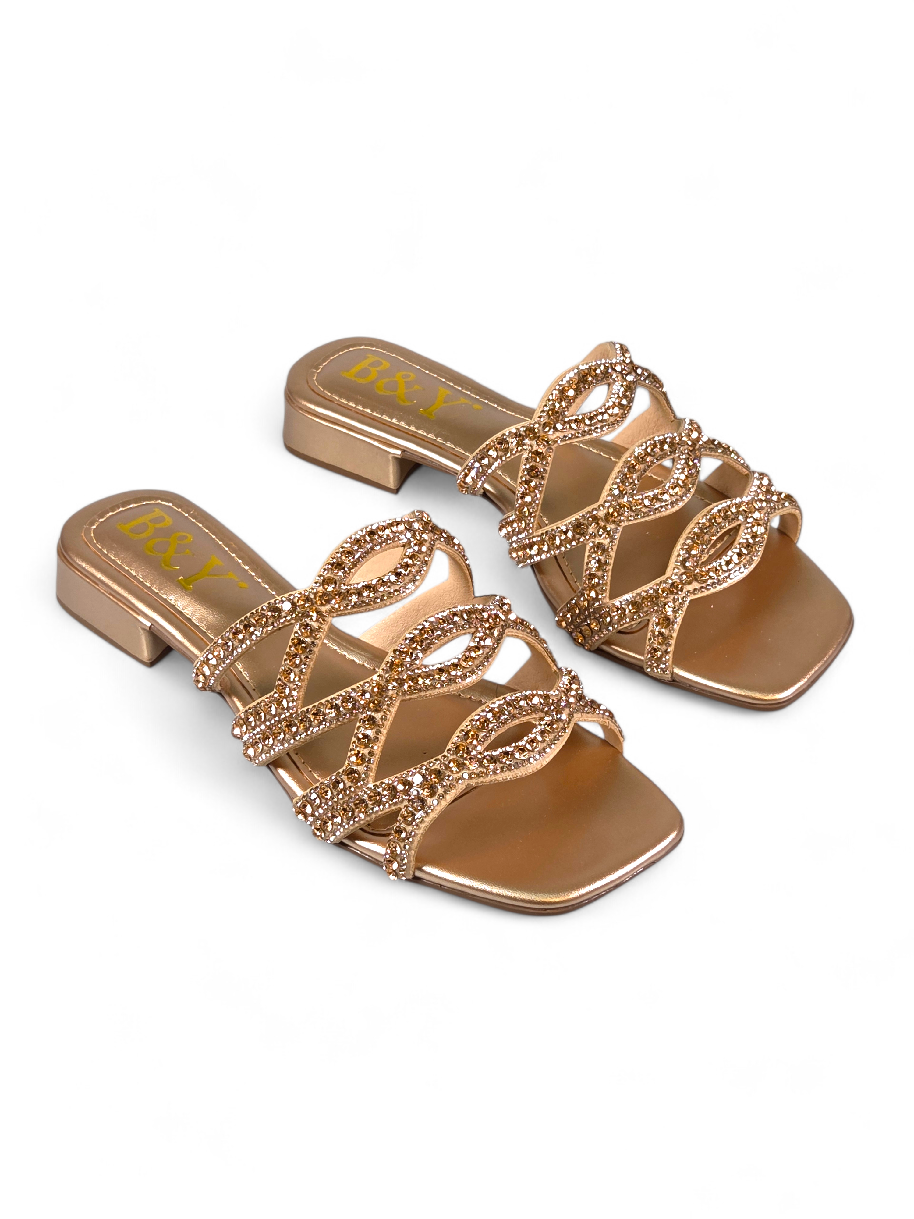 Sandália artesanal B&Y dourada com tiras ornamentais cravejadas de cristais, salto baixo e acabamento metálico, em fundo branco.