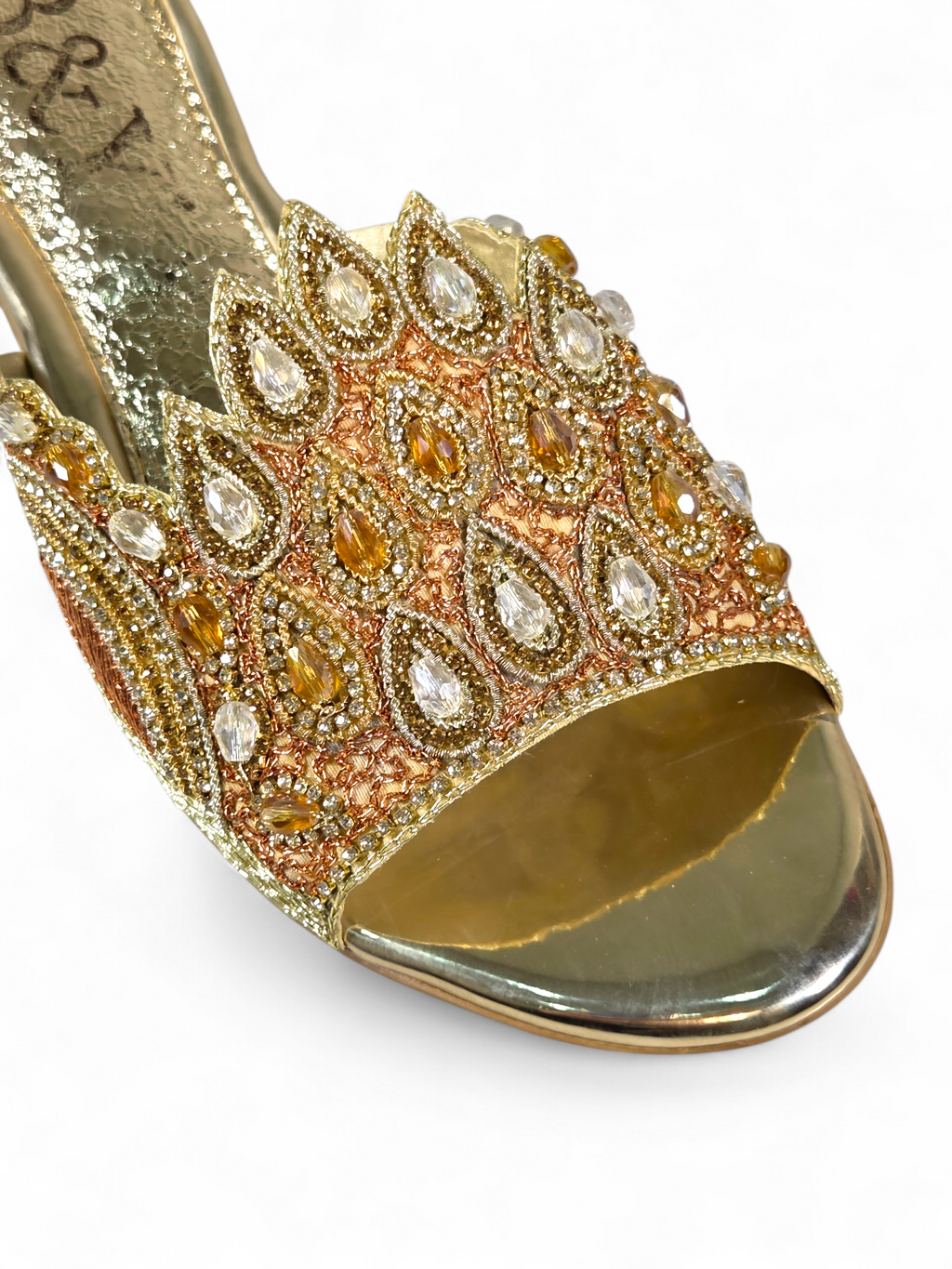 A close-up of a gold and beige high-heeled sandal with intricate beaded and crystal embellishments.