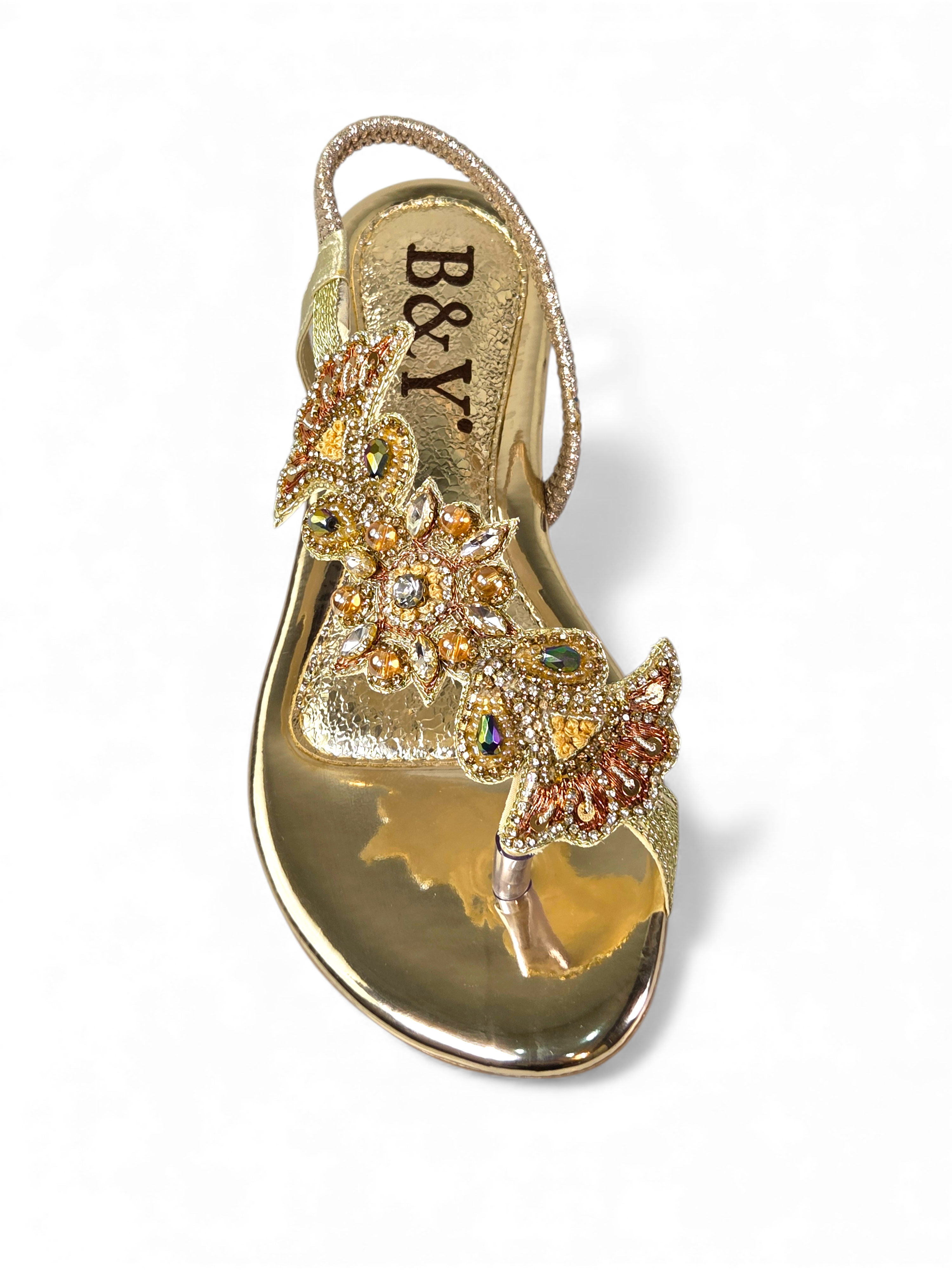 A gold-colored, ornate sandal with intricate floral and crystal embellishments.