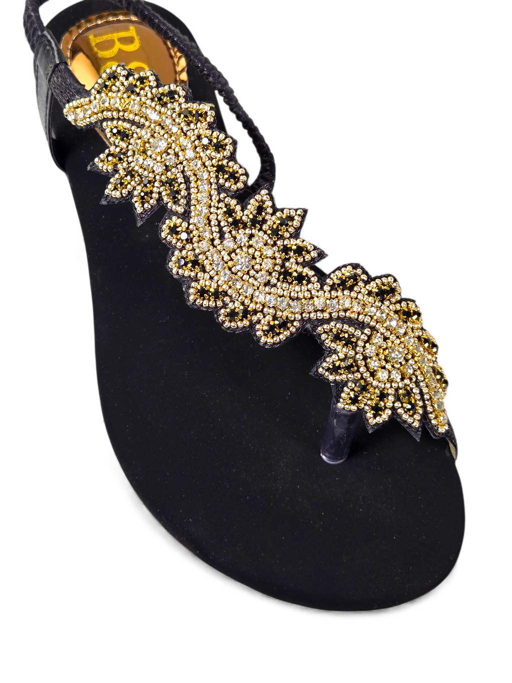 A close-up view of a black sandal with a decorative gold leaf embellishment.
