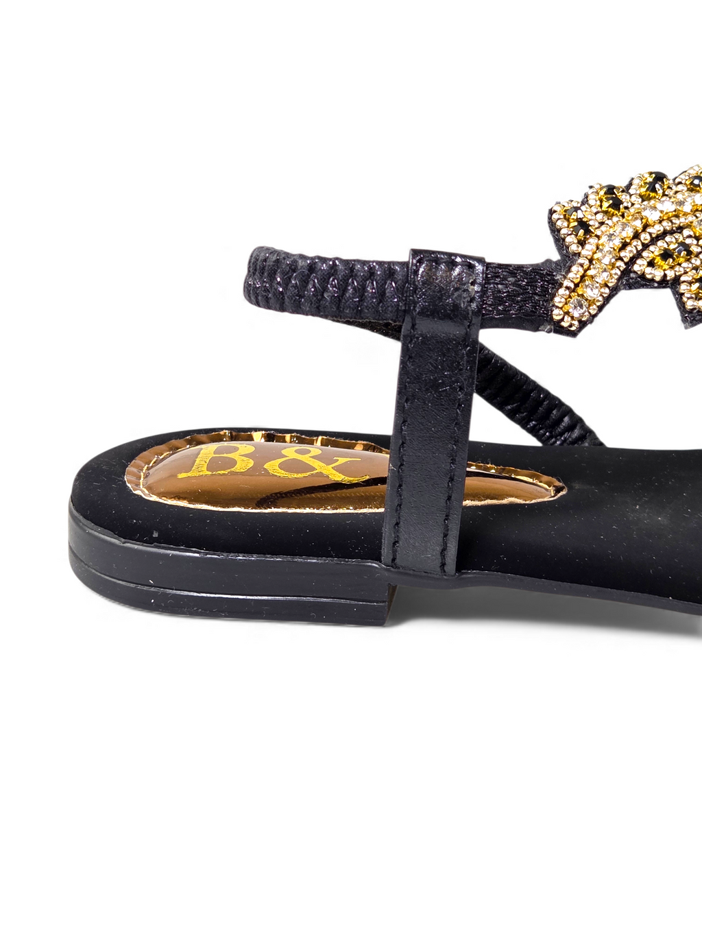 A close-up view of a black sandal with a gold and black embellished star design on the heel.