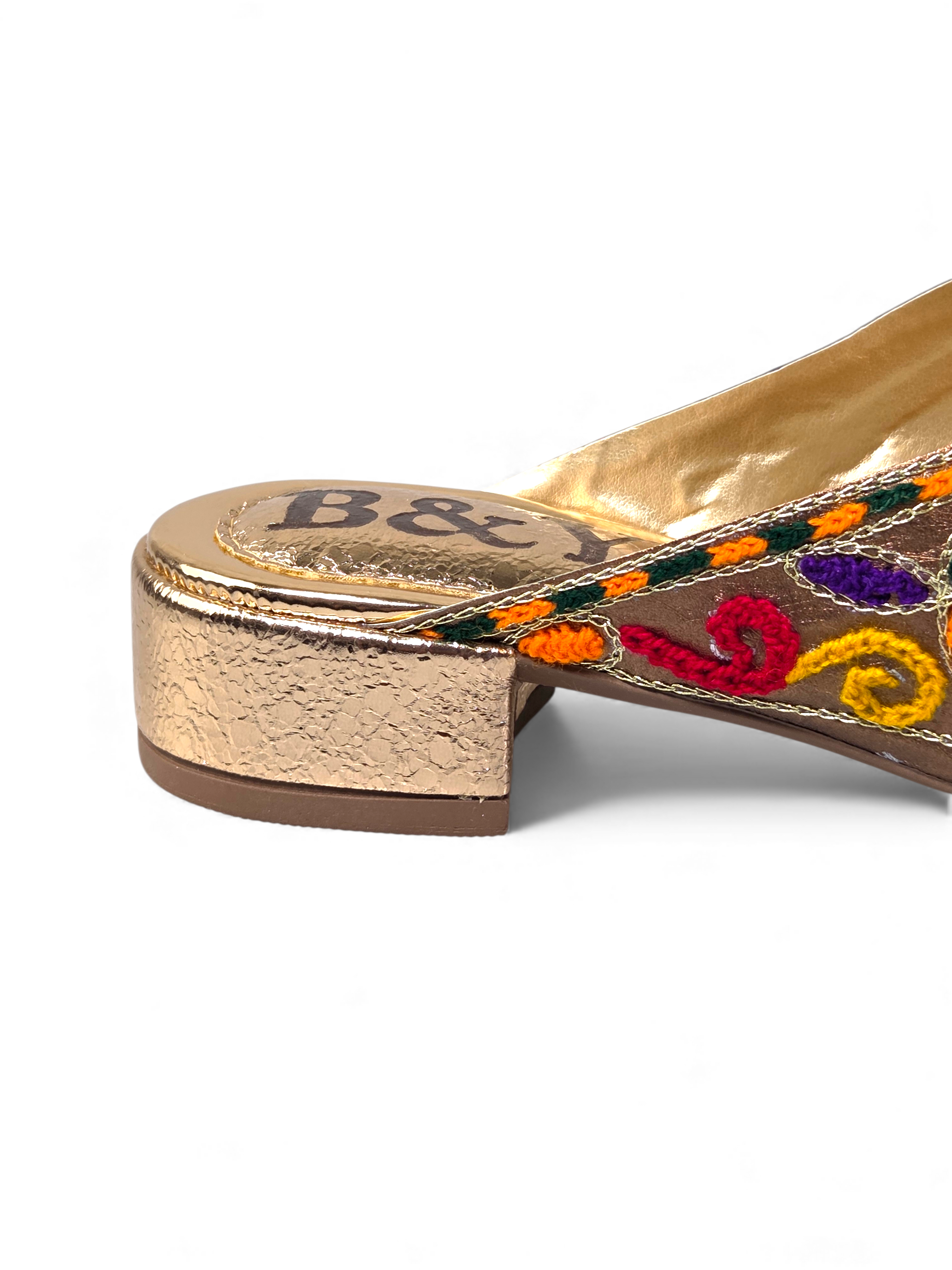 A close-up view of a gold-colored shoe with a decorative pattern on the toe and heel.