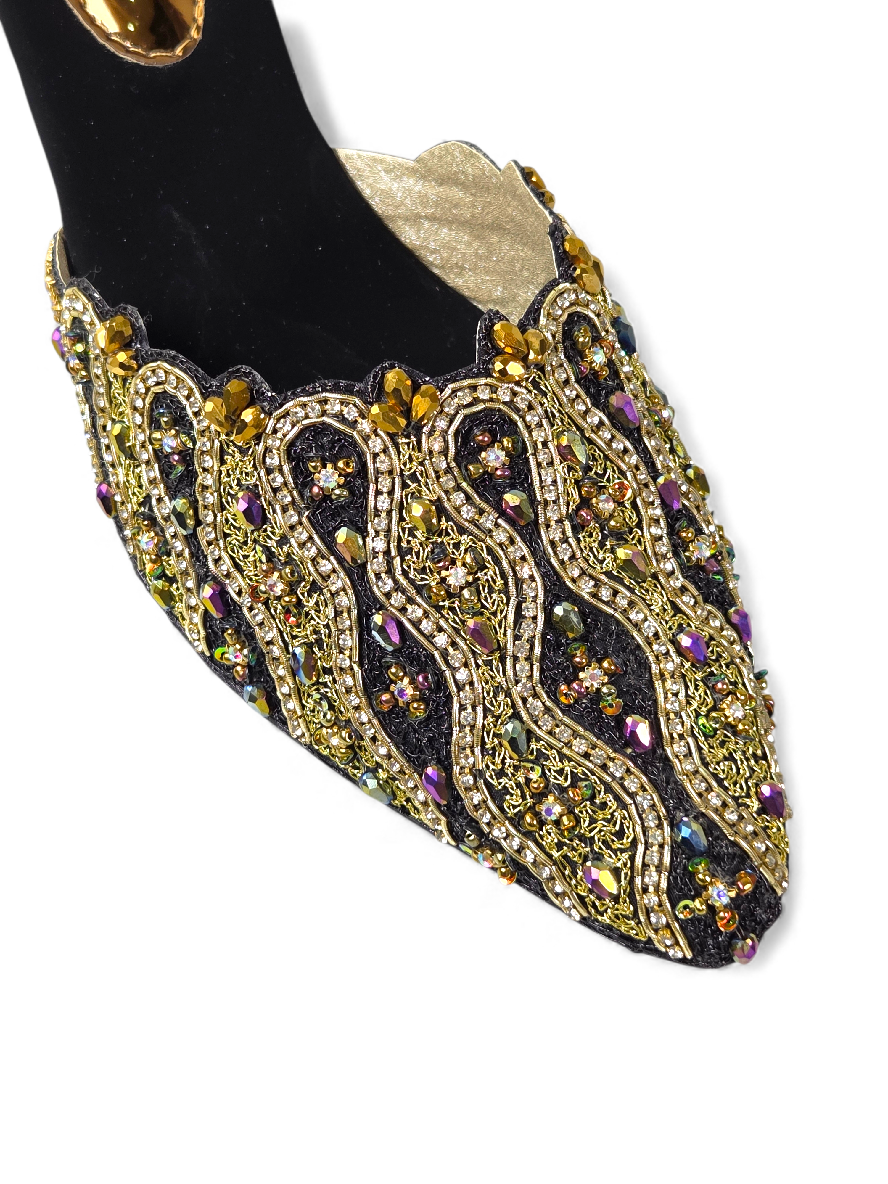 A close-up view of an ornate, embellished shoe with intricate gold and black designs, including rhinestones and sequins.