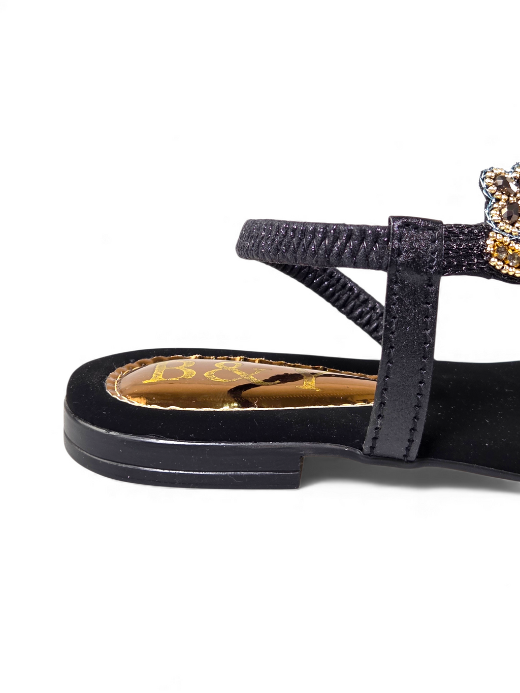 A close-up view of a black sandal with a gold-colored buckle and a black strap.