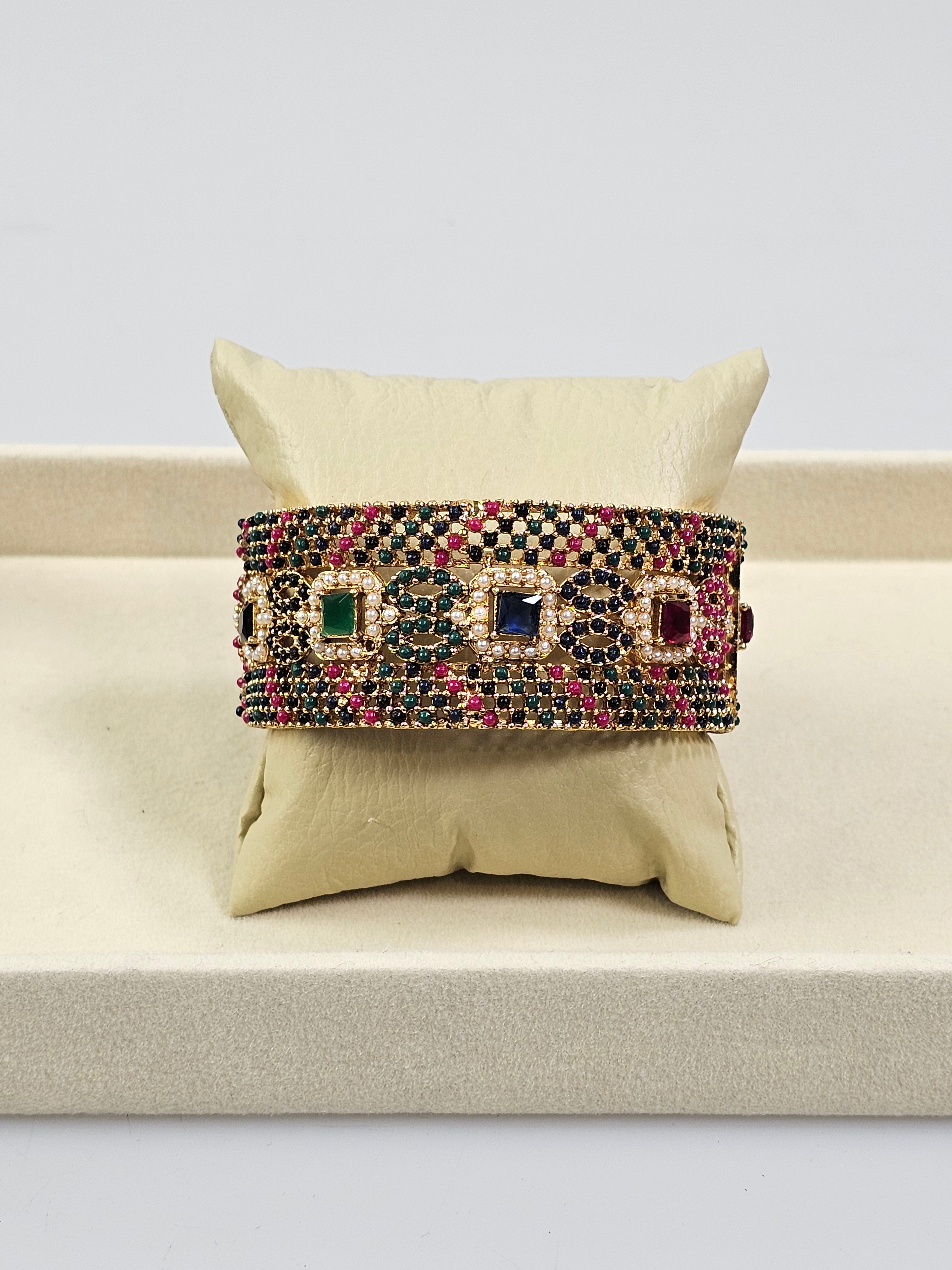 Bracelete artesanal B&Y com pedras verde-esmeralda, azul-safira, douradas e rubi, joia vibrante e elegante.